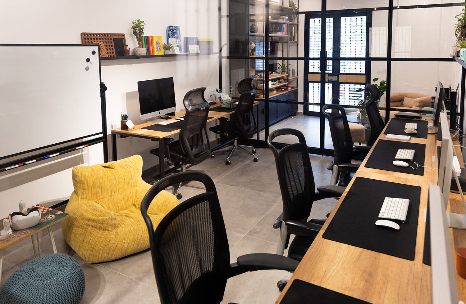 Modern office space featuring multiple workstations with computers, ergonomic chairs, a large whiteboard, and a cozy seating area with a yellow bean bag.